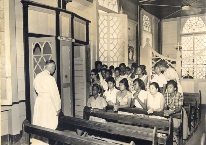 Pater Lambers, redemptorist, gaat middelbare schoolmeisjes de biecht afnemen, in de Rosakerk te Paramaribo